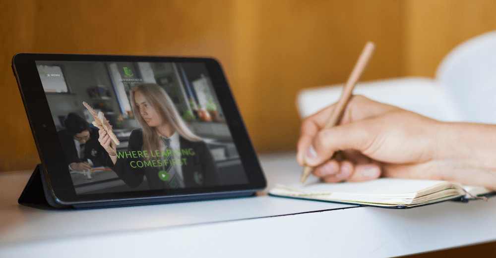 iPad on a desk next to a lady writing in a notebook